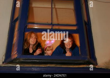 Leute, die vom Fenster im ersten Stock aus die brennenden Prozessionen der Lewes Fire Societies in Lewes in Sussex, England, am 5.. November, Guy Fawkes Night, beobachten. Stockfoto