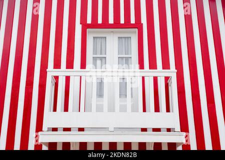Alte Holztür und ein Balkon auf dem Hintergrund der gestreiften rot-weißen Wand. Portugal Windows. Das Äußere der portugiesischen Häuser Stockfoto