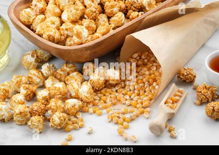 Popcorn in Holzschüssel, Maiskörner, Karamellsauce und Ölflasche auf Küchentisch. Stockfoto