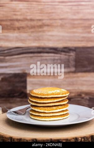 Ein großer Teller mit Pfannkuchen mit einer Gabel vor einem Holzhintergrund. Stockfoto