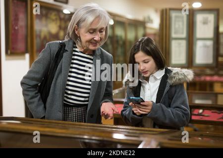 Präteen Mädchen mit Großmutter, die Telefon, um Informationen über Exponate im Museum zu finden Stockfoto