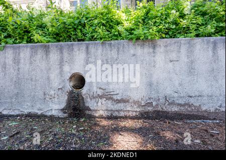 Regenwasserablauf in einem städtischen Gebiet mit Sickerwasser, das eine Betonbarriere verfärbt Stockfoto