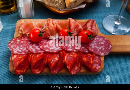 Spanische leckere Gerichte, die Würstchen und Schinken mit Tomaten am Holzschreibtisch schneiden Stockfoto