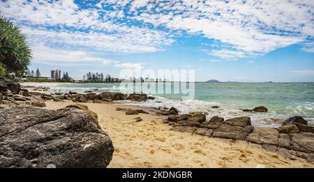 Szene mit Blick nach Norden von Alexandra Headland am Strand in Richtung Cotton Tree an der Sunshine Coast, Queensland. Felsige Landzunge, raues Meer und blauer Himmel mit Stockfoto