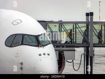 An einem Winterflughafen mit fallendem Schnee steigen Passagiere aus dem Flugzeug in den Tunnel Stockfoto