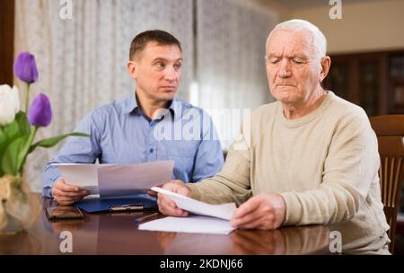 Mann, der seinem Vater beim Ausfüllen von Dokumenten hilft Stockfoto