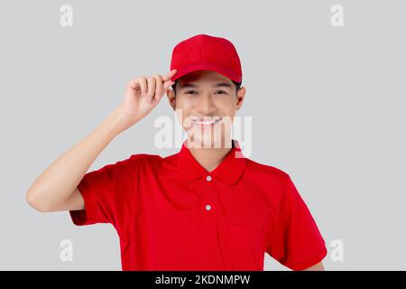 Junger asiatischer Mann in Uniform und roter Mütze steht und fängt einen Hut mit selbstbewussten isolierten weißen Hintergrund, Mitarbeiter und Versand, Kurier und Lieferung, Stockfoto