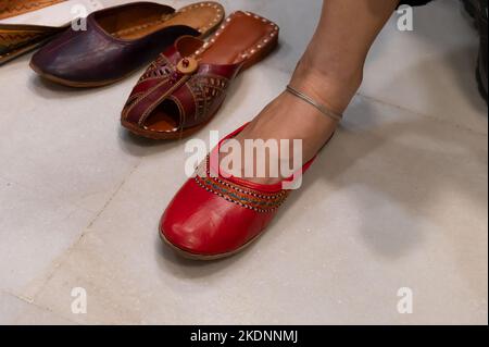 Schöne indische Frau, die ihren Fuß für das Anbringen von bunten Rajsathani Damenschuhen im Geschäft am berühmten Sardar Markt und Ghanta ghar Markt probiert. Stockfoto