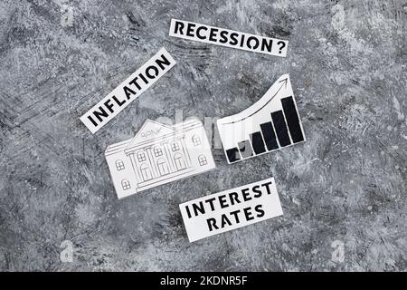 Texte zu Zinssätzen, Inflation und Rezession mit Banksymbol neben dem Diagramm mit nach oben kommenden Statistiken und wirtschaftlichen Kämpfen nach der Pandemie Stockfoto