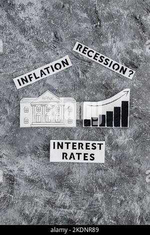 Texte zu Zinssätzen, Inflation und Rezession mit Banksymbol neben dem Diagramm mit nach oben kommenden Statistiken und wirtschaftlichen Kämpfen nach der Pandemie Stockfoto