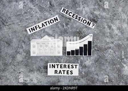 Texte zu Zinssätzen, Inflation und Rezession mit Banksymbol neben dem Diagramm mit nach oben kommenden Statistiken und wirtschaftlichen Kämpfen nach der Pandemie Stockfoto