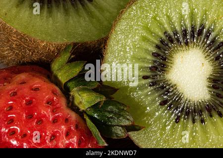 Kiwi halbiert neben einer Erdbeere in einer geschlossenen Makroebene. Stockfoto