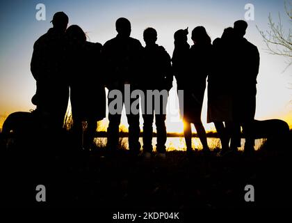 Silhouette einer Gruppe von Menschen, die den Sonnenuntergang vor einem See beobachten. Stockfoto