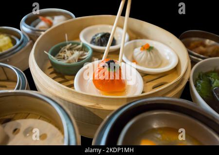 Stempelschnitt aus orangefarbenem Xiao Long bao und setzen Dim Sum auf schwarz isoliert. Stockfoto