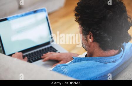 Das World Wide Web erkunden. Rückansicht eines Junggesellen, der sich mit seinem Laptop auf dem Sofa entspannt. Stockfoto