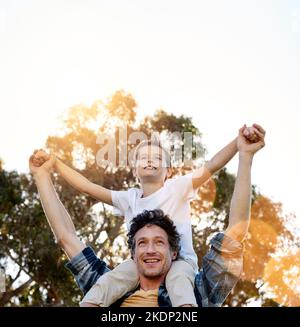 Und der amtierende Champion ist mein Sohn. Ein glücklicher Vater trägt seinen jungen Sohn auf den Schultern draußen. Stockfoto