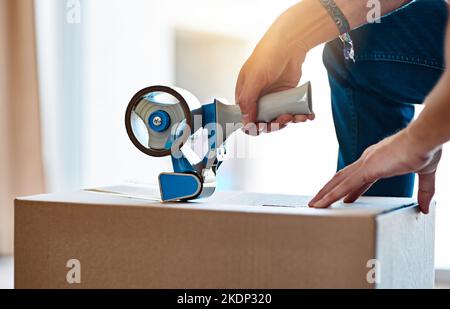 Es sind aufregende Zeiten. Ein nicht erkennbarer junger Mann, der zu Hause einen Karton mit Klebeband schließt. Stockfoto