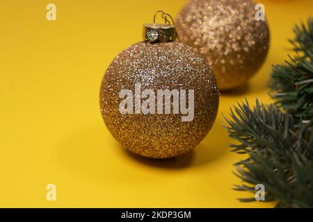 goldene Weihnachtskugeln auf gelbem Hintergrund mit grüner Kiefer Stockfoto