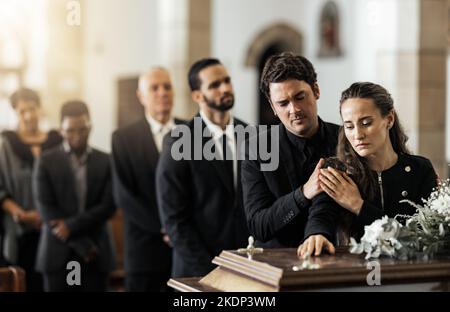 Tod, Beerdigung und Familie berühren Sarg in einer Kirche, traurig und unglücklich, während sich treffen, um Abschied zu nehmen. Kirchendienerkassette und trauriger Mann und Frau Stockfoto