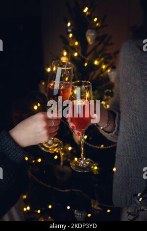 Zwei Mädchen mit einem Glas Champagner am Weihnachtsbaum. Vorderansicht. Vertikales Foto. Stockfoto