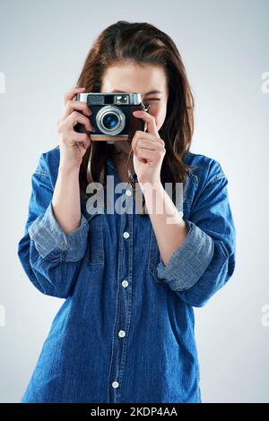 Können Sie Käse sagen, bitte. Studioportrait einer jungen Frau mit einer Vintage-Kamera vor grauem Hintergrund. Stockfoto