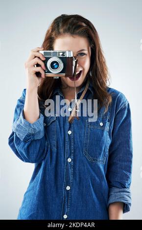 Ich liebe es, Momente in der Zeit einzufrieren. Studioportrait einer jungen Frau mit einer Vintage-Kamera vor grauem Hintergrund. Stockfoto