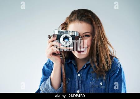 Das Leben sieht durch ein Objektiv besser aus. Studioportrait einer jungen Frau mit einer Vintage-Kamera vor grauem Hintergrund. Stockfoto