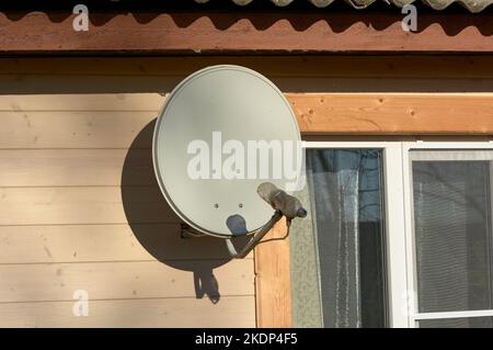 An der Wand eines Holzhauses hängt eine Satellitenschüssel Stockfoto