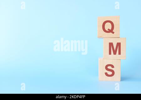 QMS oder Qualitätsmanagementsystem auf Holzblöcken auf blauem Hintergrund. Stockfoto