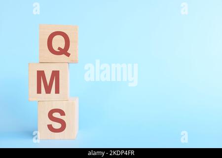 QMS oder Qualitätsmanagementsystem auf Holzblöcken auf blauem Hintergrund. Stockfoto