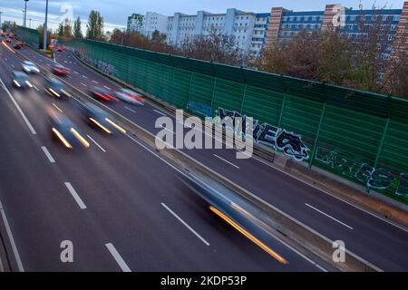 PRODUKTION - 07. November 2022, Sachsen-Anhalt, Magdeburg: Der abendliche Berufsverkehr rollt an Wohngebäuden der Landeshauptstadt Magdeburg auf der Stadtautobahn vorbei. Aufgrund der langen Belichtung hinterlassen die Lichter der Fahrzeuge Streifen auf dem Bild. In Sachsen-Anhalt fahren die meisten Menschen nach Magdeburg. Dies wird durch neue Zahlen des Staatlichen Statistikamtes bestätigt. Demnach hatte die Landeshauptstadt 2021 mit knapp 18.000 arbeitenden Menschen die höchste Pendlerbilanz in Sachsen-Anhalt. Das bedeutet, dass mit rund 53.000 deutlich mehr Erwerbstätige pendeln Stockfoto