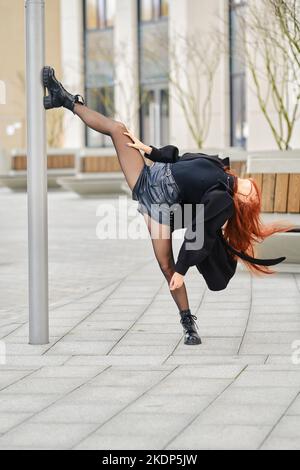 Die flexible junge Frau zeigt sich gespalten, indem sie ihren Fuß auf einen Stock setzt Stockfoto