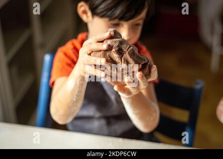 Nahaufnahme der Kinderhände, die den Schokoladenteig kneten Stockfoto