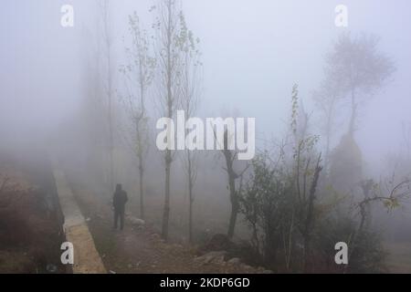 Srinagar, Indien. 07.. November 2022. Ein Mann geht während eines nebligen Wetters am Stadtrand von Srinagar entlang des Hügels. Regen setzte sich fort, die Ebenen zu schlagen, während obere Reichweiten Schneefall erhielten, da der Wettermann bis November 11 mehr nasses Wetter in Jammu und Kaschmir vorhersagte. Kredit: SOPA Images Limited/Alamy Live Nachrichten Stockfoto