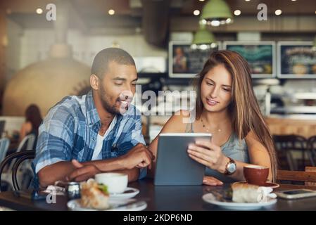 Cafe Connections. Ein junges Paar, das ein digitales Tablet benutzt, während es in einem Café sitzt. Stockfoto