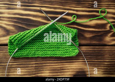 Angefangen hat das Stricken auf den Stricknadeln, mit dem Garn auf dem rustikalen Holztisch, mit den grünen Zweigen des Weihnachtsbaums. Wir stricken warme Kleidung mit unserem eigenen h Stockfoto