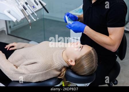 Der Arzt zeigt bunte Gummibänder auf den Hosenträger des Patienten. Mann mit Drahtspangen an den Zähnen, der in der Klinik einen zahnärztlichen Eingriff durchmacht. Gebiss Stockfoto