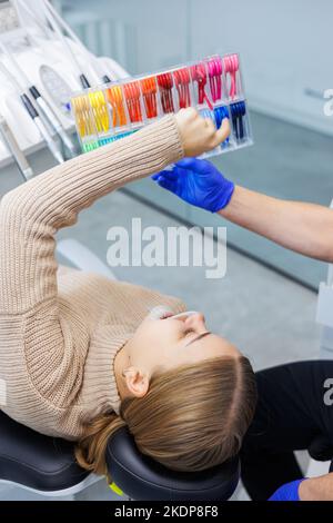 Der Arzt zeigt bunte Gummibänder auf den Hosenträger des Patienten. Mann mit Drahtspangen an den Zähnen, der in der Klinik einen zahnärztlichen Eingriff durchmacht. Gebiss Stockfoto