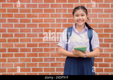 Thai asiatische Schule Mädchen teen glücklich Lächeln in Uniform Griff Buch und Schultasche mit Kopieplatz Stockfoto