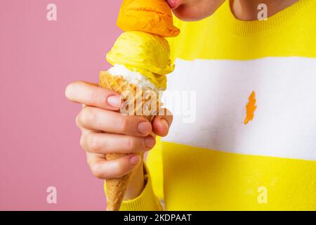 Nicht erkennbare Frau, die Eiscreme-Kegel mit drei Kugeln mit unterschiedlichem Geschmack isst. Schmutzige gefrorene Dessertfleck auf der Kleidung. Isoliert Stockfoto