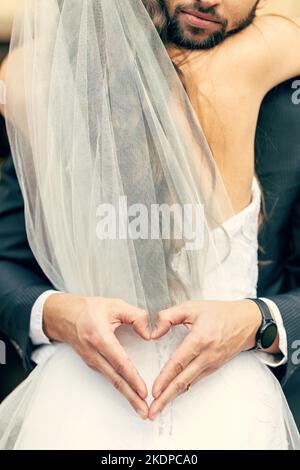 Hand, Herz und Braut und Bräutigam umarmen sich bei ihrer Hochzeit, freuen sich und entspannen sich, während sie einen intimen Moment teilen. Hände, Liebe und Paar feiern ihre Stockfoto