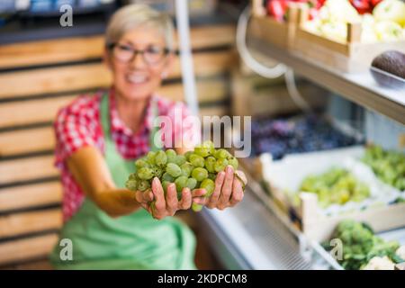 Frau arbeitet im Obst- und Gemüseladen. Sie untersucht Trauben. Stockfoto