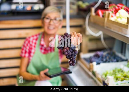 Frau arbeitet im Obst- und Gemüseladen. Sie untersucht Trauben. Stockfoto