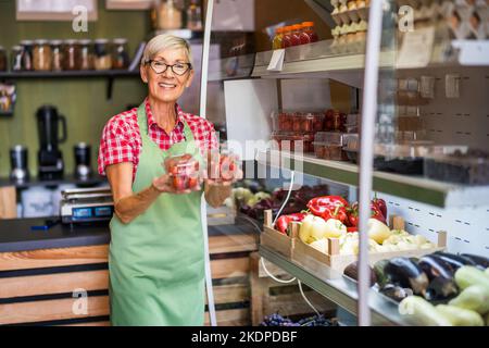 Reife Frau arbeitet im Obst- und Gemüseladen. Sie prüft Waren. Stockfoto