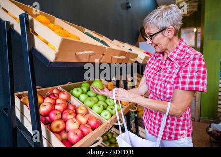 Reife Frau, die im Obst- und Gemüseladen Waren kauft. Stockfoto