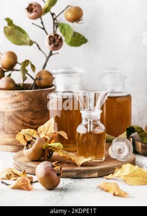 Hausgemachter Mislar-Sirup oder Saft in drei Apothekengläsern mit frischen reifen Früchten auf Holzschneidebrett. Konzept der alternativen Medizin. Stockfoto