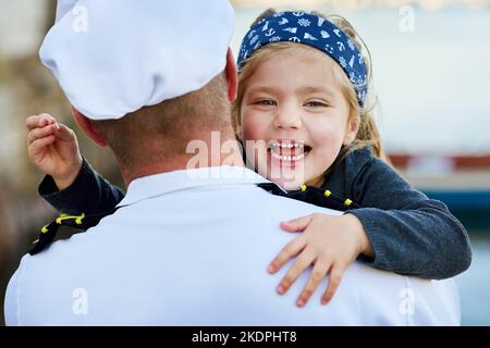 Hat dich aussehen lassen. Rückansicht eines Vaters in einer Marineinuniform, der sein glückliches kleines Mädchen umarmt. Stockfoto