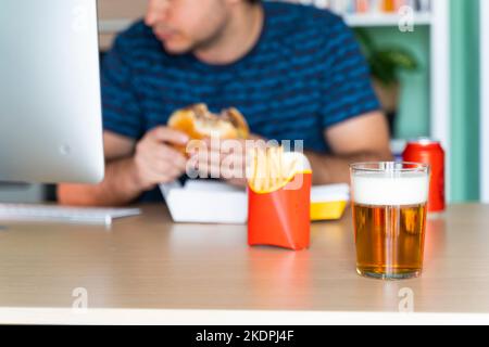 Mann, der vor dem Computer in seinem Büro Fastfood isst Stockfoto