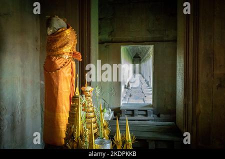 Eine alte Statue ist in orangefarbenen Gewändern an einem buddhistischen Schrein in Angkor Wat in Kambodscha gekleidet. Stockfoto