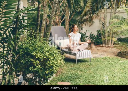 Junge Frau entspannt sich auf einer Sonnenliege im Garten. Meditation im Garten. Stockfoto